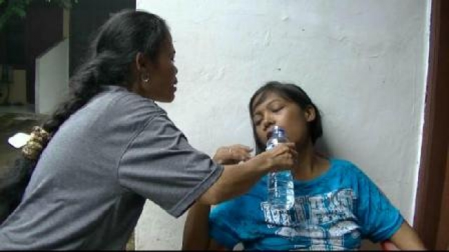 Tetangga tengah memberikan air minum mineral kepada Frida, penderita penyakit ginjal di rumahnya, RT 05/01 Kelurahan Rengas, Ciputat Timur-Kota Tangsel