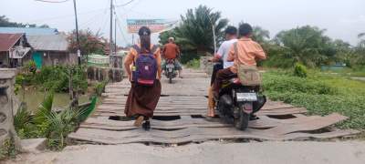 Anak sekolah melintasi jembatan Kayu Besar yang rusak parah.